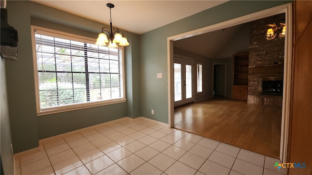 unfurnished dining area featuring an inviting chandelier, a fireplace, light hardwood / wood-style flooring, lofted ceiling, and french doors