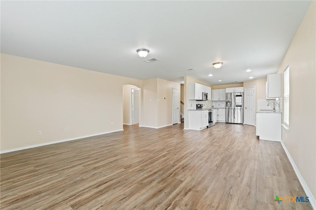 9305 Devonshire Ct, Killeen, TX 76542 - unfurnished living room with arched walkways, light wood finished floors, baseboards, a sink, and recessed lighting