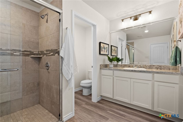 bathroom with wood-type flooring, vanity, toilet, and a shower with door