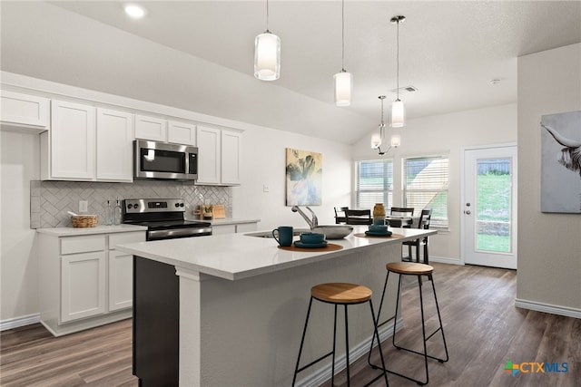 kitchen with appliances with stainless steel finishes, pendant lighting, white cabinets, lofted ceiling, and a kitchen island with sink