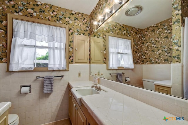 bathroom with vanity, a wainscoted wall, toilet, tile walls, and wallpapered walls