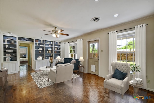 living area with crown molding, baseboards, a ceiling fan, and visible vents