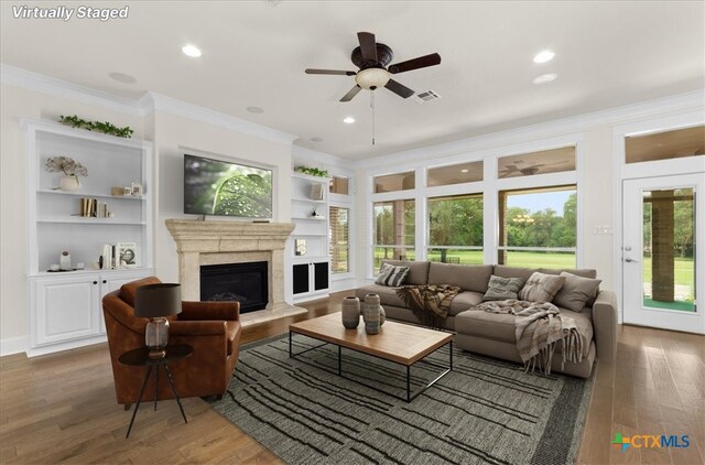 2901 Chisholm Trl, Salado, TX 76571 - living area with crown molding, wood finished floors, a ceiling fan, built in features, and a fireplace with raised hearth