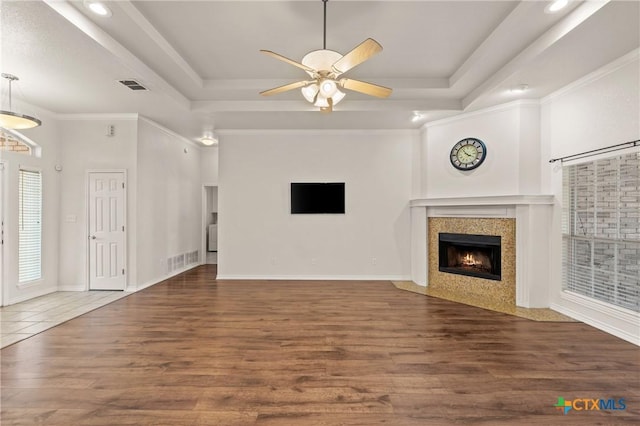 unfurnished living room with ceiling fan, dark hardwood / wood-style flooring, a tray ceiling, and ornamental molding