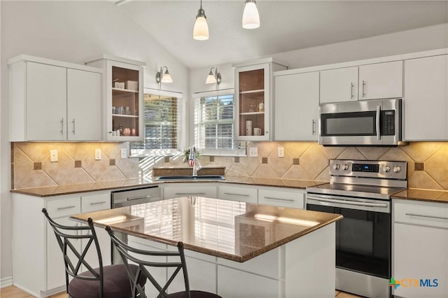 kitchen with appliances with stainless steel finishes, a kitchen breakfast bar, vaulted ceiling, a kitchen island, and sink