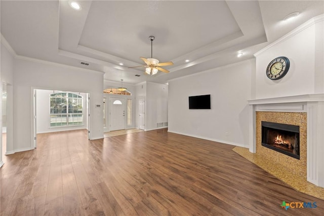 unfurnished living room with hardwood / wood-style floors, ornamental molding, a raised ceiling, ceiling fan, and a tile fireplace