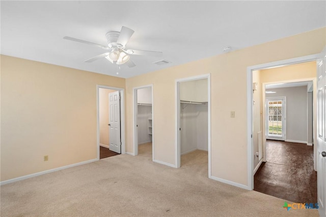 unfurnished bedroom with visible vents, a walk in closet, baseboards, carpet floors, and a ceiling fan