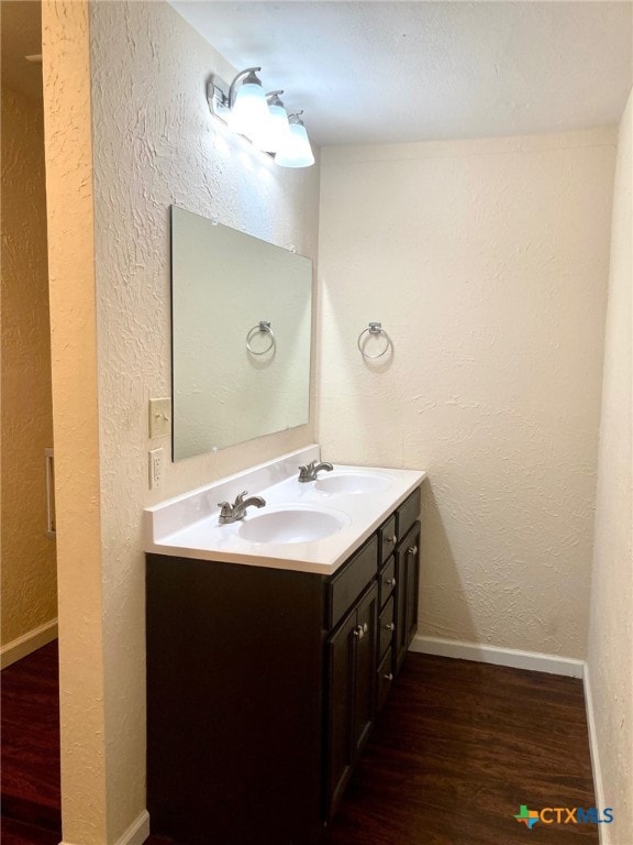 full bathroom featuring double vanity, wood finished floors, baseboards, and a sink