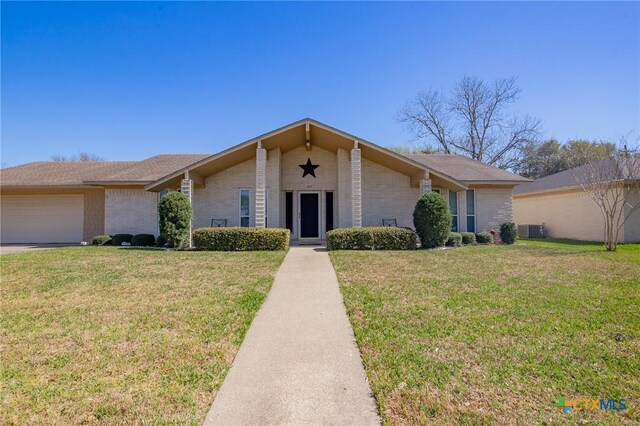 mid-century home with a garage, a front yard, cooling unit, and brick siding