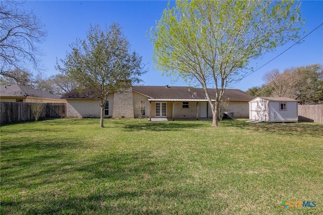 back of house featuring a lawn, french doors, a storage shed, a fenced backyard, and an outbuilding