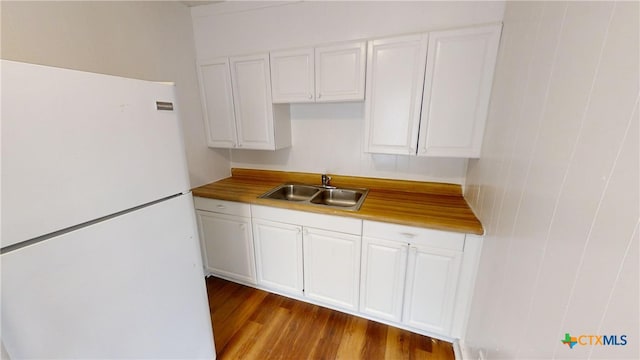 kitchen with white cabinets, light hardwood / wood-style flooring, sink, and white refrigerator