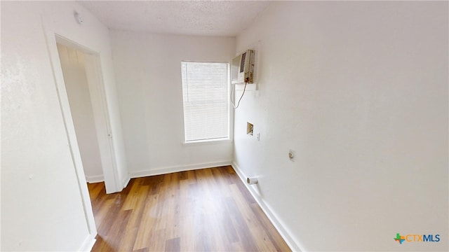 unfurnished room with a wall unit AC, a textured ceiling, and hardwood / wood-style flooring