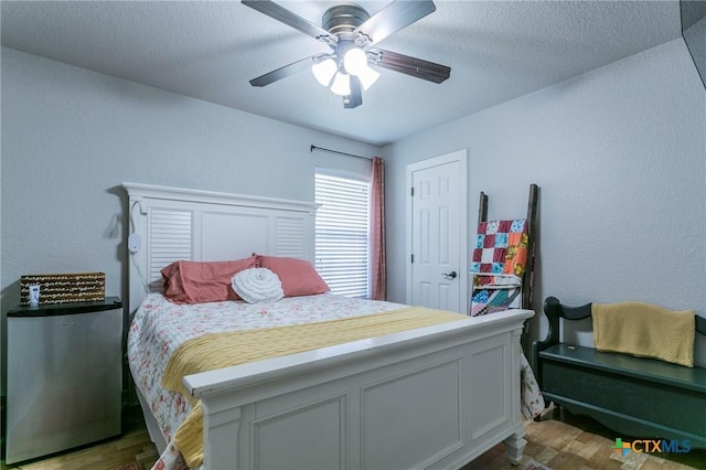 bedroom with ceiling fan, hardwood / wood-style floors, stainless steel fridge, and a textured ceiling