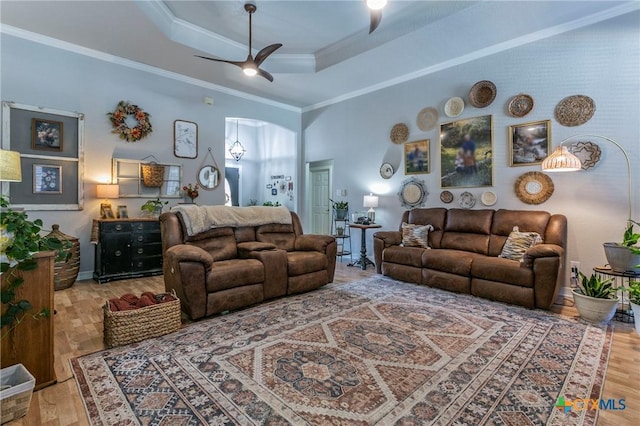 living room featuring a raised ceiling, ceiling fan, ornamental molding, and wood-type flooring