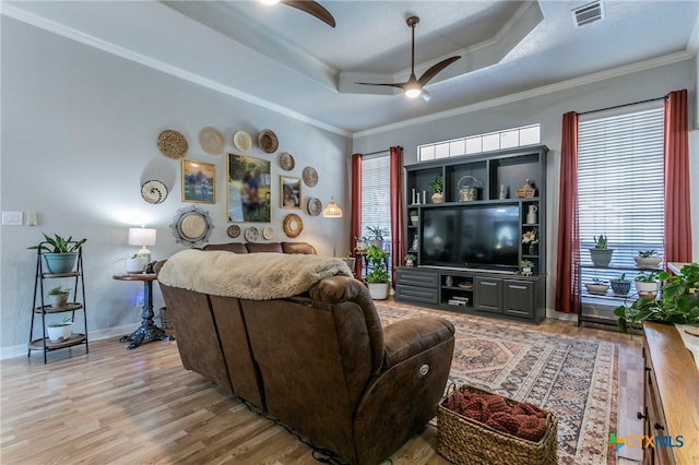 living room with ceiling fan, light hardwood / wood-style floors, ornamental molding, and a raised ceiling