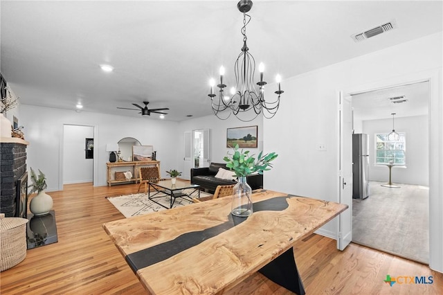 dining area with light wood finished floors, visible vents, a fireplace, and a ceiling fan