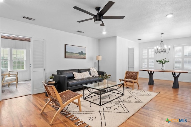 living area featuring baseboards, visible vents, light wood finished floors, a textured ceiling, and ceiling fan with notable chandelier