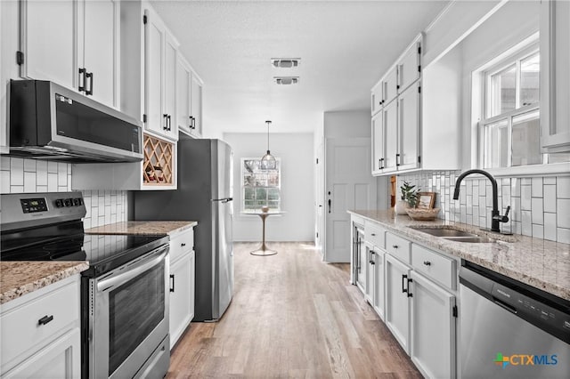 kitchen with a sink, stainless steel appliances, light wood-style floors, white cabinets, and light stone countertops