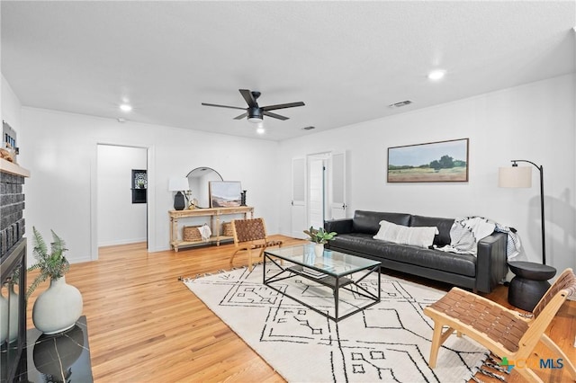 living room featuring light wood finished floors, visible vents, a brick fireplace, recessed lighting, and a ceiling fan