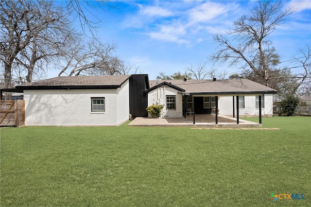 rear view of house featuring fence, a yard, a shingled roof, brick siding, and a patio area