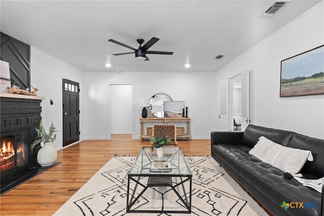 living area with visible vents, baseboards, recessed lighting, a brick fireplace, and light wood-type flooring