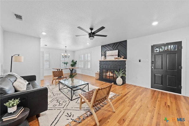 living room featuring a brick fireplace, light wood-style flooring, baseboards, and visible vents