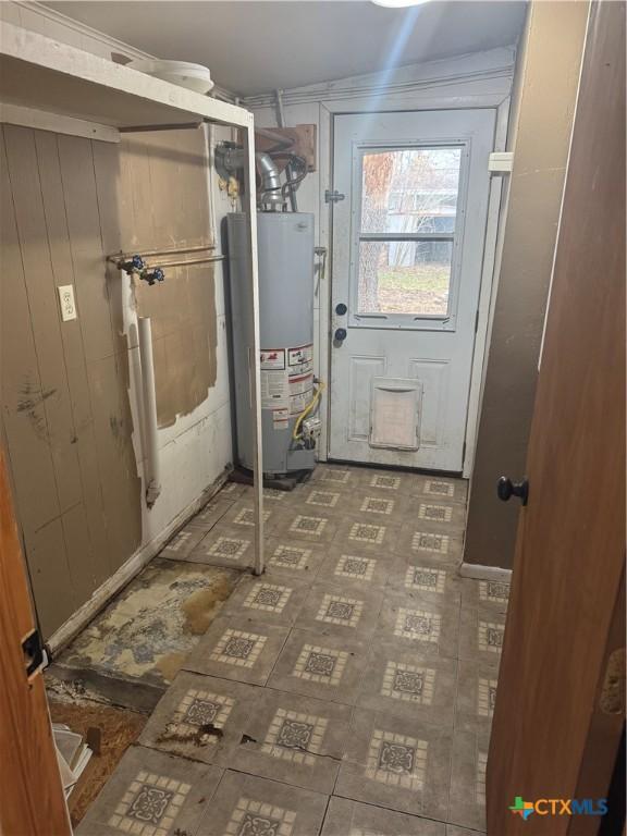 doorway to outside featuring gas water heater and wood walls