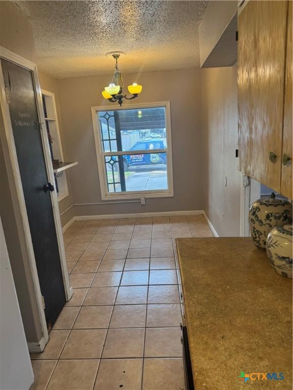 unfurnished dining area featuring light tile patterned floors, a notable chandelier, and a textured ceiling