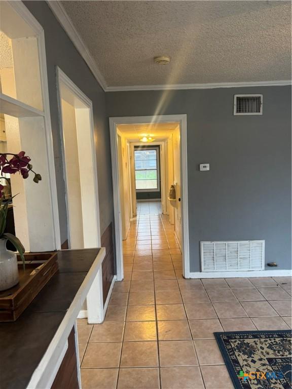 hallway with ornamental molding, a textured ceiling, and light tile patterned flooring