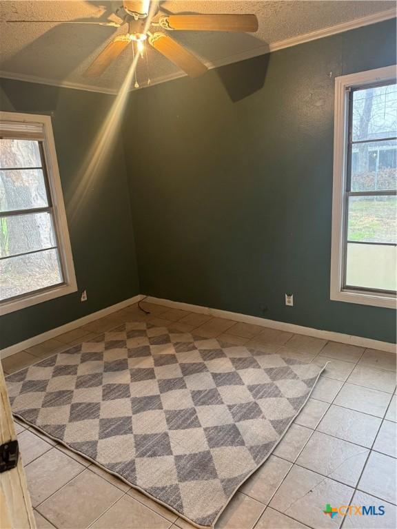 tiled spare room featuring ceiling fan, ornamental molding, and a textured ceiling