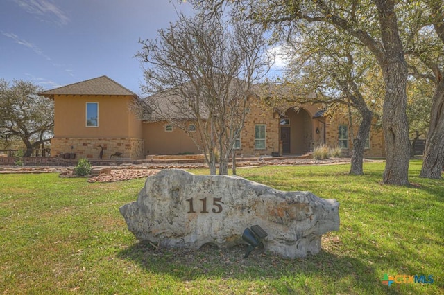 exterior space with stone siding, a front yard, and stucco siding