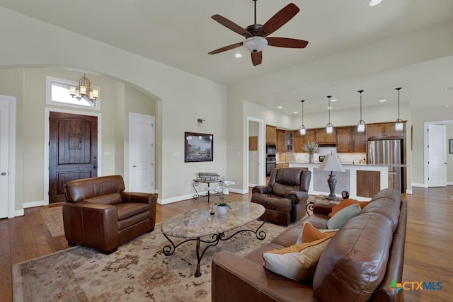 living area with baseboards, arched walkways, wood finished floors, and ceiling fan with notable chandelier