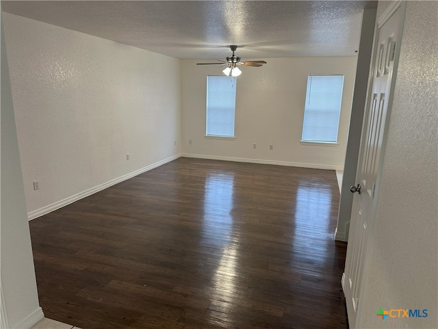 unfurnished room with dark wood-type flooring, a ceiling fan, a textured ceiling, baseboards, and a textured wall