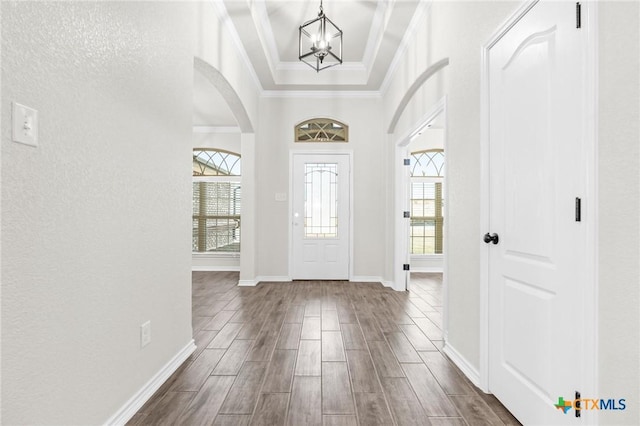 entryway with a raised ceiling, ornamental molding, and an inviting chandelier