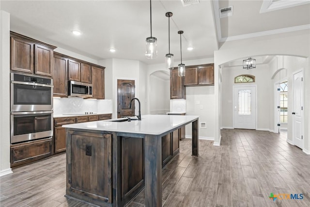 kitchen with dark brown cabinetry, sink, decorative light fixtures, a center island with sink, and stainless steel appliances