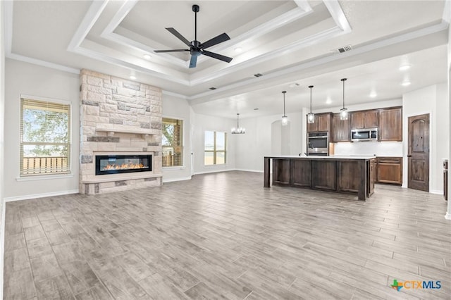 unfurnished living room featuring ornamental molding, a stone fireplace, a raised ceiling, and ceiling fan with notable chandelier