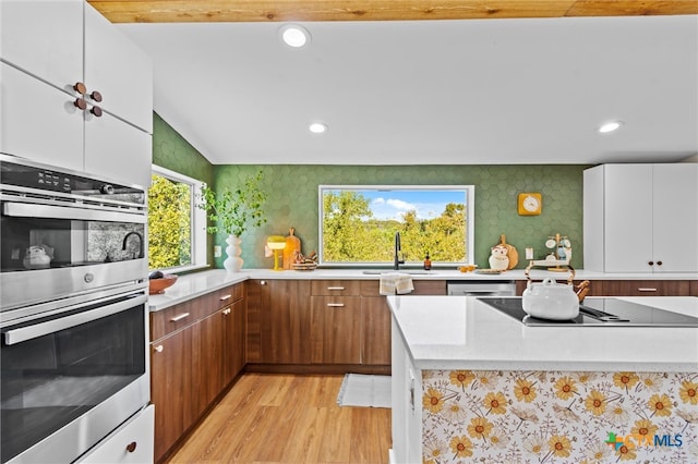 kitchen with light hardwood / wood-style floors, vaulted ceiling, sink, double oven, and white cabinetry