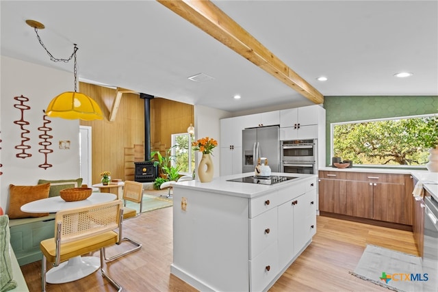 kitchen with a center island, a wood stove, hanging light fixtures, white cabinetry, and appliances with stainless steel finishes