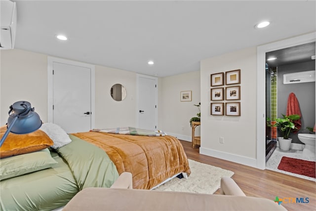 bedroom featuring hardwood / wood-style flooring, a wall mounted AC, and connected bathroom