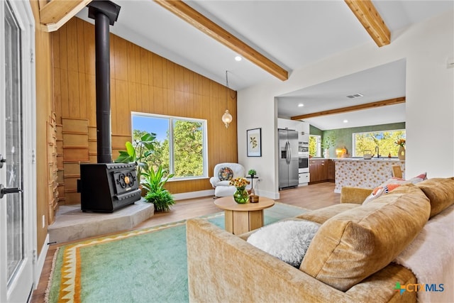 living room featuring a wood stove, lofted ceiling with beams, light hardwood / wood-style flooring, and wood walls