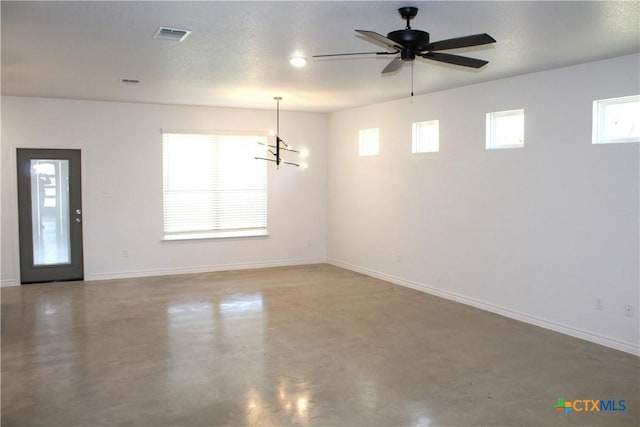 unfurnished room featuring a healthy amount of sunlight, ceiling fan with notable chandelier, and concrete flooring