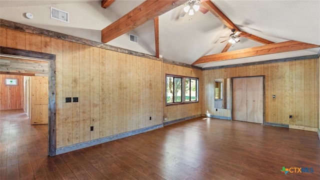 empty room featuring wood walls, dark wood-type flooring, ceiling fan, and vaulted ceiling with beams