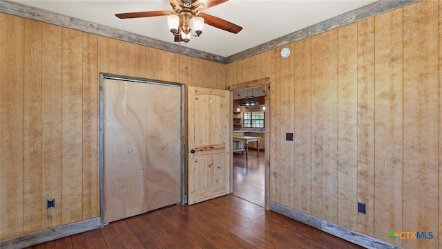 unfurnished bedroom with dark wood-type flooring, a closet, wooden walls, and ceiling fan