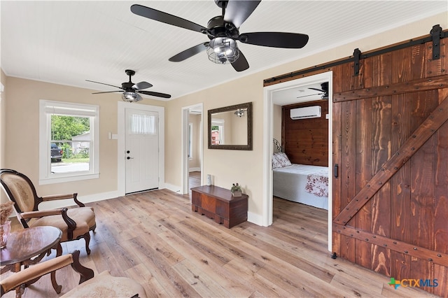 living area featuring a wall mounted AC, a barn door, ceiling fan, crown molding, and light hardwood / wood-style flooring