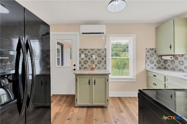 kitchen with a wall unit AC, green cabinets, black appliances, and light wood-type flooring