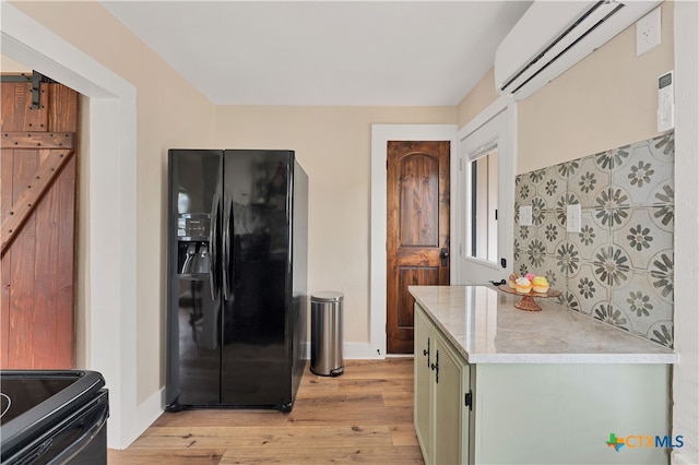 kitchen with black appliances, a barn door, green cabinetry, a wall mounted air conditioner, and light hardwood / wood-style flooring