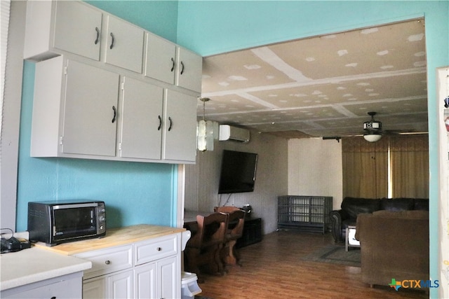 kitchen featuring dark hardwood / wood-style flooring, a wall mounted AC, ceiling fan, pendant lighting, and white cabinetry