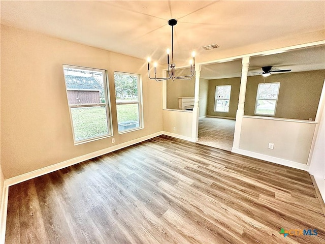 unfurnished dining area featuring ceiling fan with notable chandelier and wood-type flooring