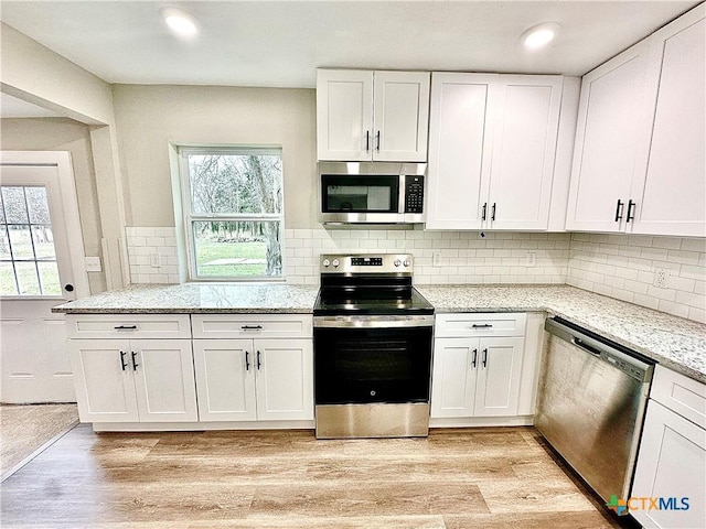 kitchen featuring stainless steel appliances, white cabinets, light hardwood / wood-style flooring, decorative backsplash, and light stone countertops