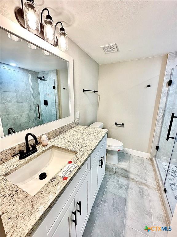 bathroom featuring toilet, a textured ceiling, a shower with door, and vanity